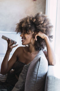 Smiling woman sending voicemail through mobile phone at home