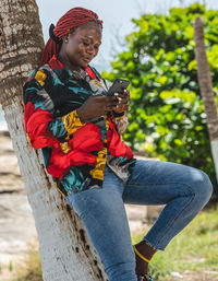 African woman leaning against a coconut tree and sending message with her mobile in accra ghana