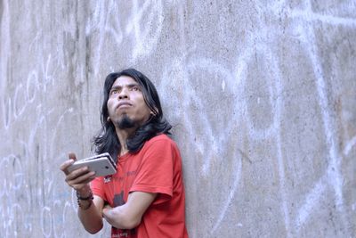 Man using mobile phone while standing against wall