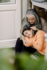 Happy senior woman stroking granddaughter while sitting at doorway