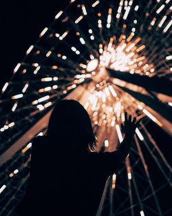 Low angle view of silhouette girl against illuminated ferris wheel at night in amusement park