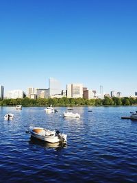 Boats in river by buildings against clear blue sky