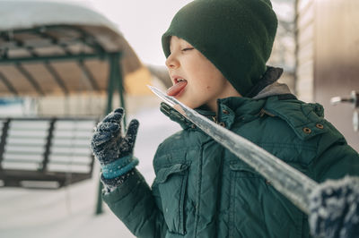 Mischievous boy licking icicle in winter