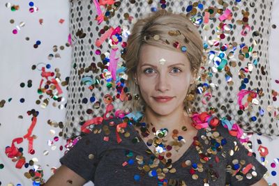 Portrait of woman lying amidst multi colored confetti on bed at home