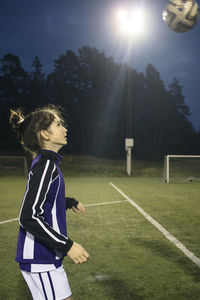 Side view of girl playing with soccer ball on field against trees
