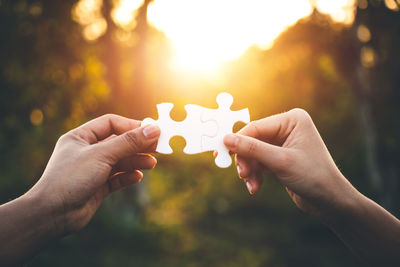 Cropped hands of women holding jigsaw pieces during sunset