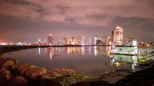 Illuminated buildings by river against sky in city at night