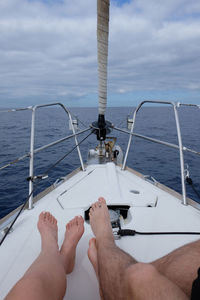 Low section of couple sailing on sea against sky