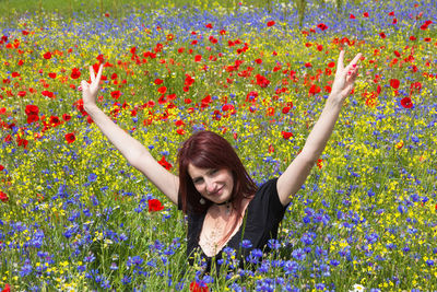 Portrait of smiling woman with arms raised amidst flowers on field