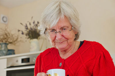 Senior woman holding coffee cup sitting at home