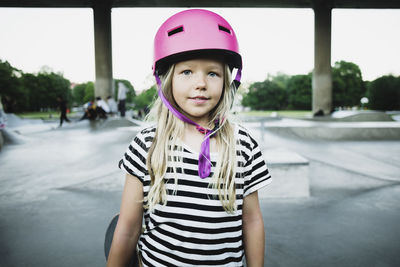 Portrait of smiling girl wearing pink helmet standing at skateboard park