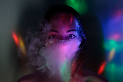 Close-up portrait of young woman holding multi colored fiber optic and smoke