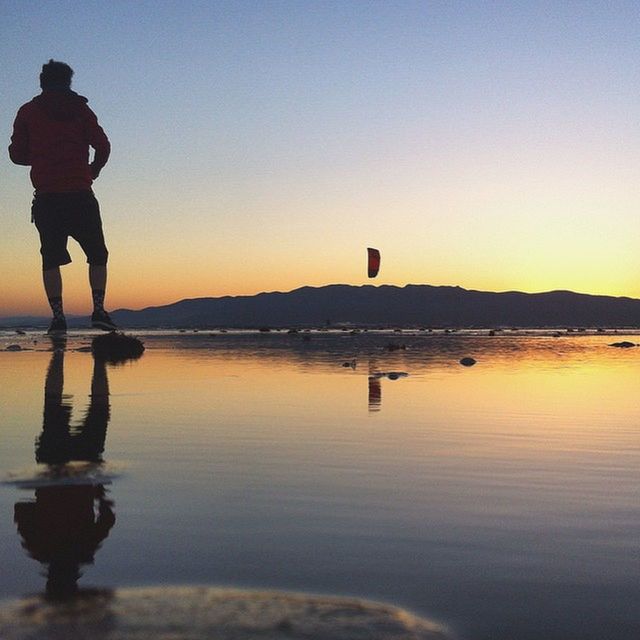 water, sunset, lifestyles, leisure activity, clear sky, silhouette, standing, scenics, tranquil scene, tranquility, men, copy space, reflection, beauty in nature, rear view, sky, nature, lake