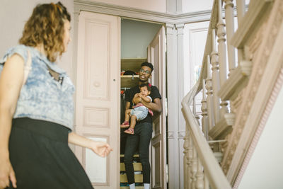 Young man looking at woman while carrying daughter at doorway