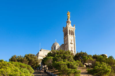 Low angle view of trees and building against clear blue sky