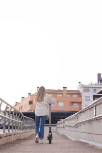 Backwards view of young woman riding an e-scooter around the city park going up the ramp 