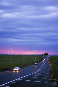 Road passing through field against cloudy sky