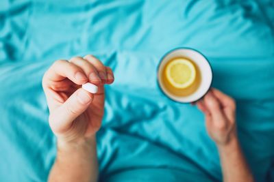 Low section of person holding coffee cup on bed