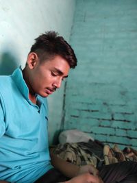 Young man looking away while sitting against wall