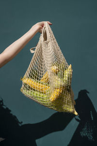 Hand of woman holding corn in mesh bag in front of wall