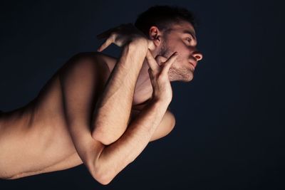 Side view of shirtless young man against black background