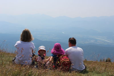 Rear view of people sitting on mountain against sky