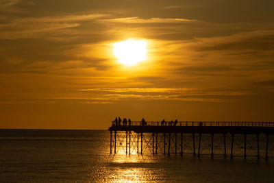 Silhouette pier over sea against sky during sunset