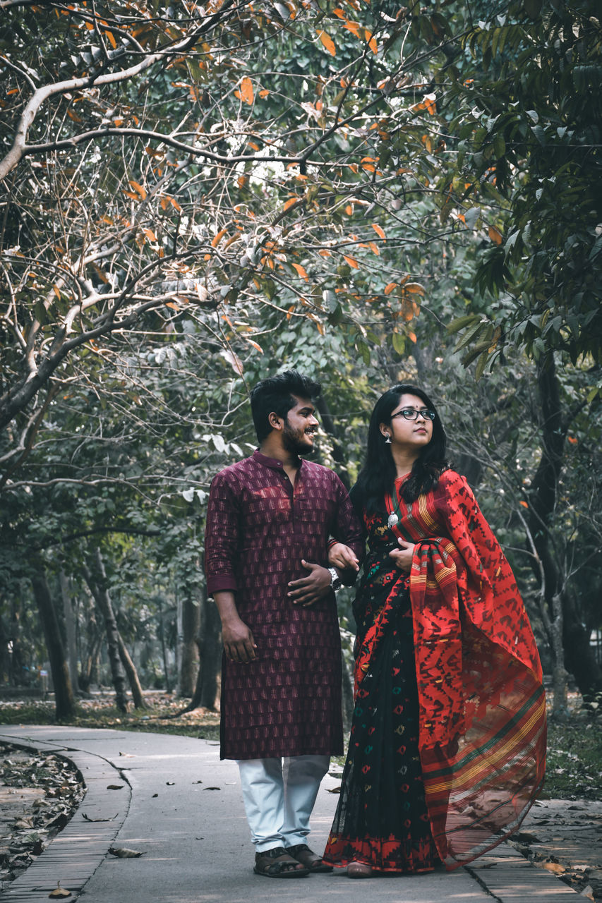 two people, young adult, tree, women, plant, young women, clothing, togetherness, adult, traditional clothing, nature, standing, full length, people, red, young men, front view, holding, couple - relationship