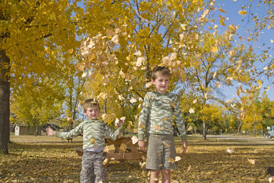 Brothers standing amidst leaves during autumn