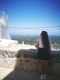 Woman standing by built structure against clear sky