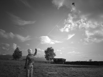 Rear view of person standing on field against cloudy sky