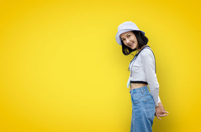 Portrait of young woman standing against yellow background