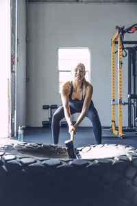 Determined woman hitting tire with sledgehammer while exercising in gym