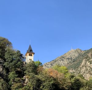 Low angle view of trees and buildings against clear blue sky