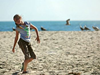 Happy girl dancing on sand at beach against sea during sunny day
