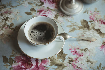 Cup with coffee on table with flower tablecloth