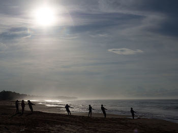 Silhouette people standing on beach against sky during sunset