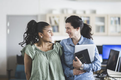 Smiling teenage high school student looking at teacher standing in computer lab