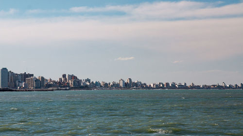 Sea by buildings in city against sky