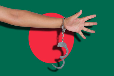 Cropped hand of person wearing handcuffs against flag