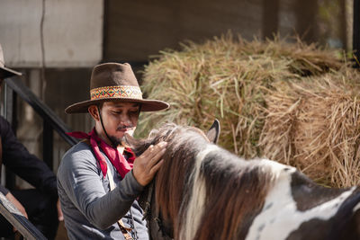 In an outdoor barn, one man dressed as a cowboy trains his horse to run in a circle around him.