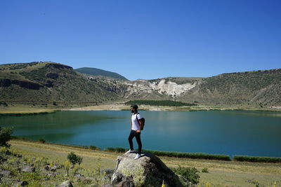 Woman standing on rock by lake against clear sky