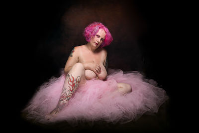 Portrait of young woman with pink petals against black background