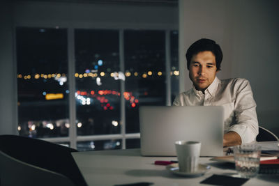 Confident businessman using laptop while sitting at desk in creative workplace