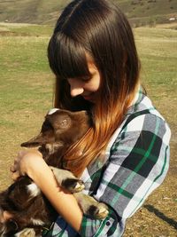 Teenage girl holding kid goat on field