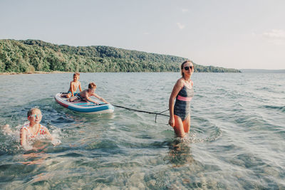 Mom woman mother riding kids children on paddle sup surfboard in lake water. 