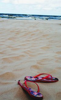 Close-up of shoes on beach against sky