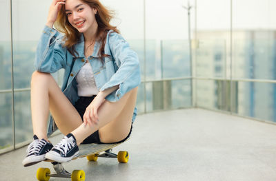 Portrait of a smiling young woman sitting on skateboard
