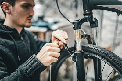 A young man pulls a brake cable on the handlebars of a bicycle.