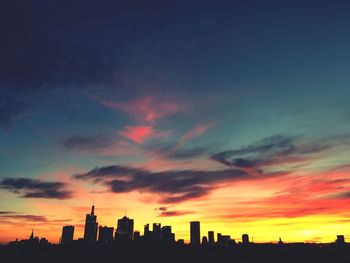 Silhouette of buildings against cloudy sky at sunset